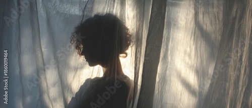 Silhouette of a woman behind sheer curtains, illuminated by soft light.