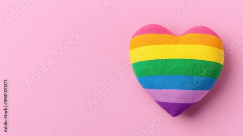 Plush rainbow striped heart shape textile representing LGBTQ pride resting on a bright pink surface