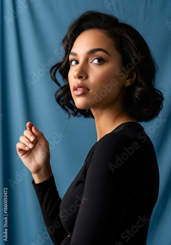 Beautiful woman in black top posing against a blue draped fabric studio background