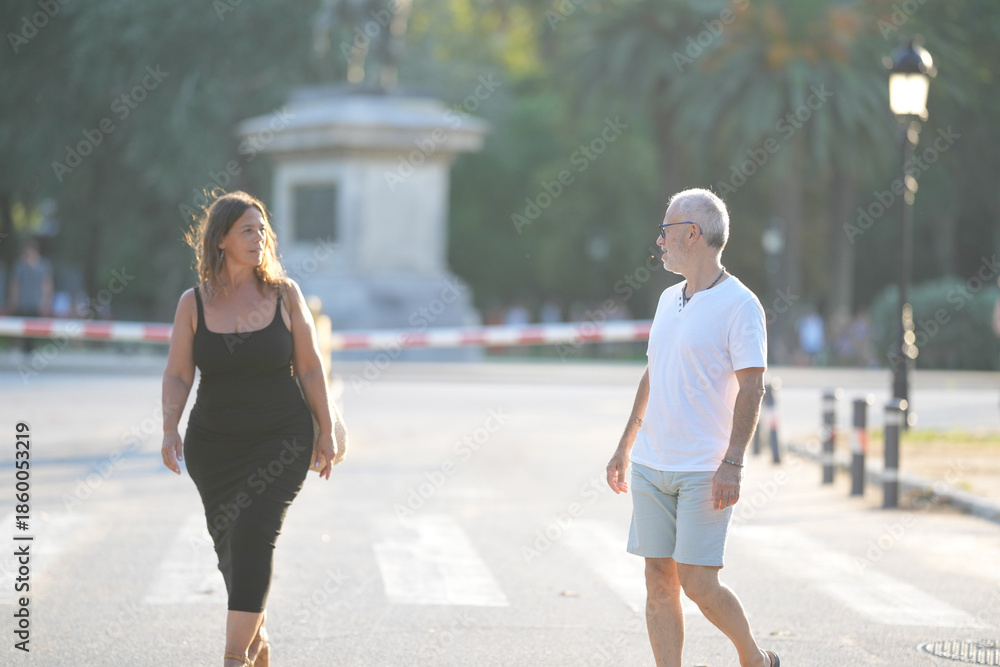 Fototapeta premium A man and a woman are walking down a street. The man is wearing a white shirt and shorts