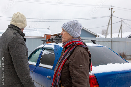 elderly woman stands in her yard with her car and adult son in the background.