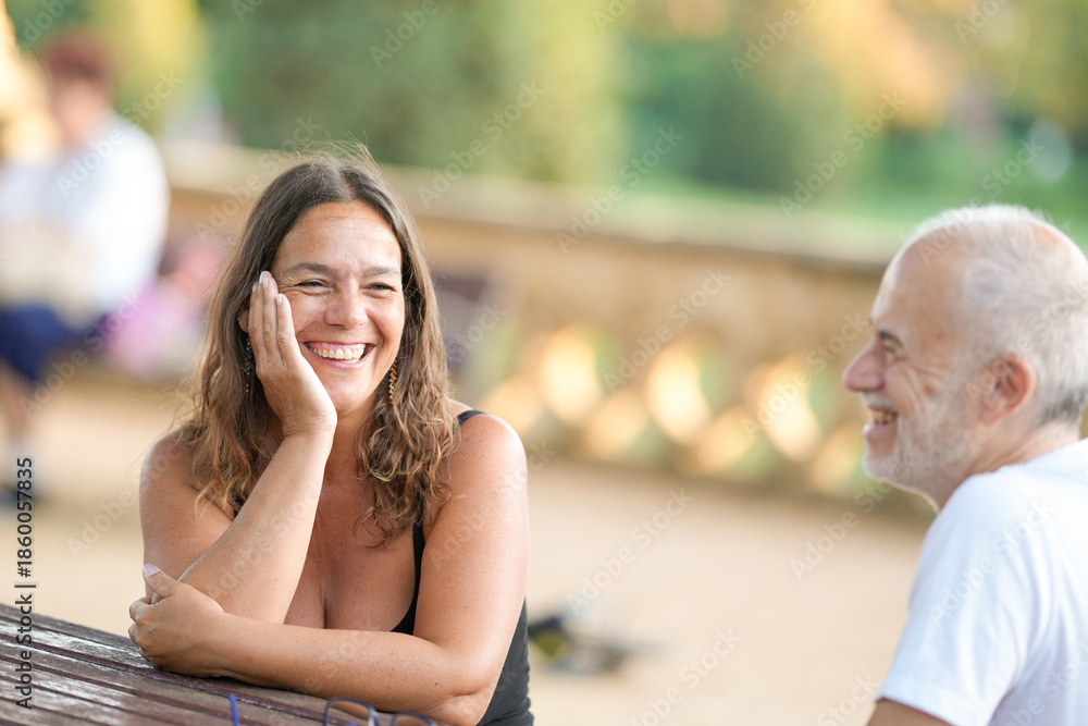 Naklejka premium A woman is sitting at a table with a man. She is smiling and laughing. The man is smiling back at her. Scene is happy and friendly