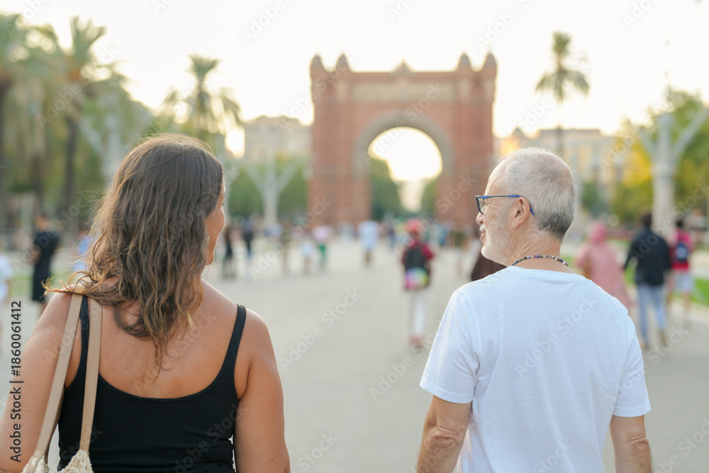 Naklejka premium A man and a woman are walking down a street in a city. The man is wearing a white shirt and the woman is wearing a black tank top. They are both carrying handbags. The scene is lively