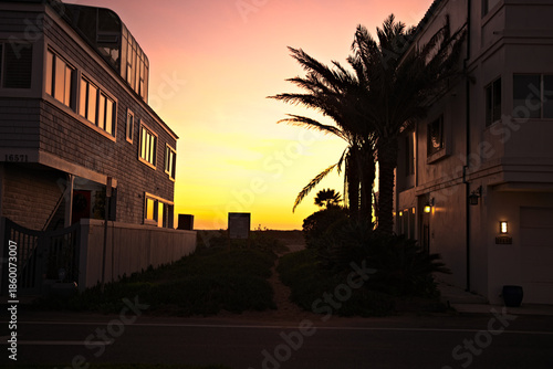 Beach access path framed by coastal homes and palm trees at sunset in Sunset Beach, California, glowing with warm golden evening light.