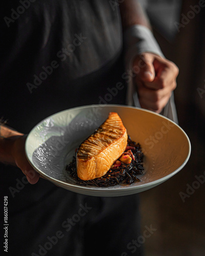 Grilled salmon fillet served by chef on dark background with elegant restaurant presentation