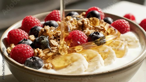 Close-up of a vibrant, healthy breakfast bowl featuring yogurt, granola, fresh berries, banana, and a golden drizzle of honey.
