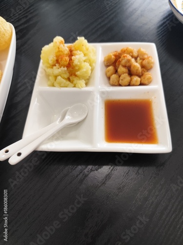 Pani puri is served on a white ceramic plate with side dishes of mashed potatoes, chickpeas, and sweet sauce.