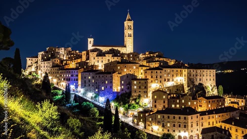 Illuminated hilltop medieval town in tuscany, italy at night with a prominent church tower against a dark blue sky, 4k