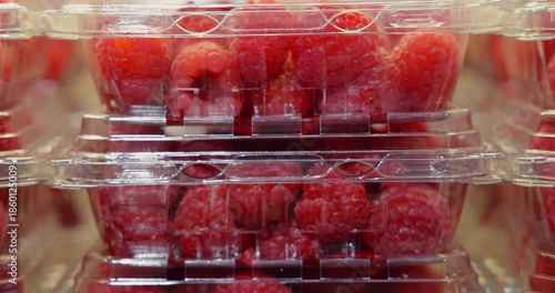 Hand stacks fresh raspberries in plastic containers within a bright supermarket produce section. Healthy eating, grocery shopping, and fresh fruit concept.