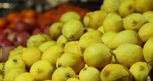 Bright yellow lemons piled high at a vibrant market stall. Fresh citrus produce for healthy eating. Slow motion, high frame rate footage.