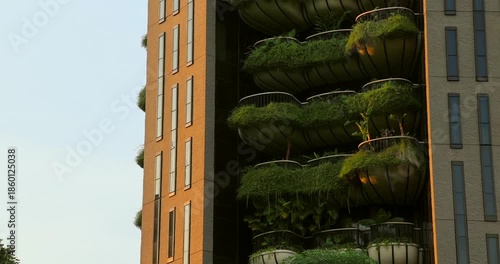 Modern building features green balconies with lush plants. Sustainable architecture and urban greening concept. Warm sunlight illuminates facade.
