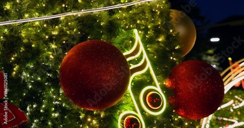 Decorated Christmas tree with glitter baubles, glowing lights, and neon musical note at night. Festive holiday season, joyful mood, slow motion, high frame rate footage.