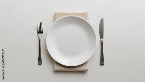 Minimalist overhead view of a clean white dinner plate centered over a small beige cloth napkin flanked precisely by a silver fork on the left and a sharp knife on the right