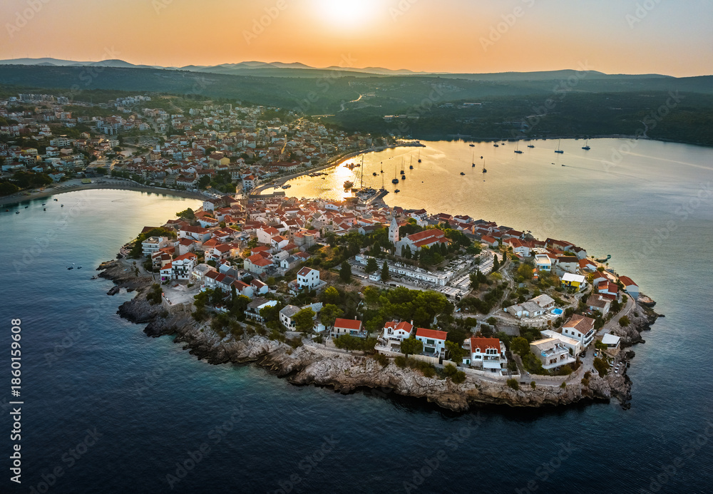 Fototapeta premium Primosten, Croatia - Aerial view of Primosten peninsula and old town on a sunny summer morning in Dalmatia, Croatia. Blue and golden sky at sunrise on the Adriatic sea coast