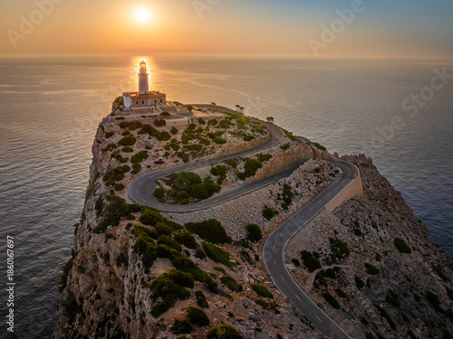 Mallorca, Spain - Aerial view of the Lighthouse and serpentine road at Cap de Formentor at sunrise with warm sunlight, clouds and blue sky