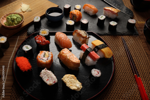 High-quality close-up of fresh assortment sushi rolls served on a dark plate, featuring vibrant colors, fresh fish, laid on slate board bamboo mat chopsticks