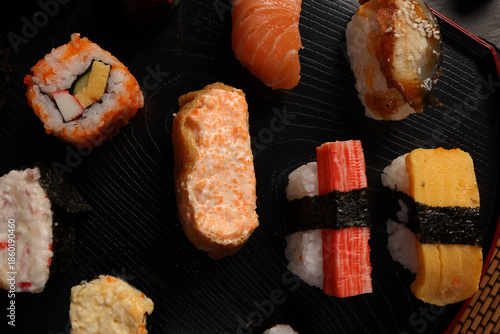 High-quality close-up of fresh assortment sushi rolls served on a dark plate, featuring vibrant colors, fresh fish, laid on slate board bamboo mat chopsticks