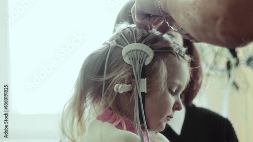 Close-up of nurse attaching contact pads to Electroencephalography electrode cap on head of 4 years old Caucasian child during brain activity diagnostic test in medical clinic. Mother parent
