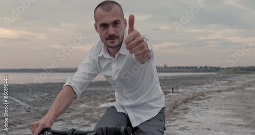 Cautious man pedals through slippery shoreline carrying full briefcase on front bar. Encouraging man signals thumbs-up while navigating challenging terrain