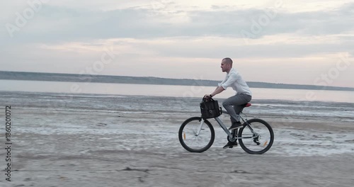 Focused guy raises body slightly off seat while cycling along uneven coastal path. Determined man stabilizes bicycle absorbing bumps under warm seaside breeze
