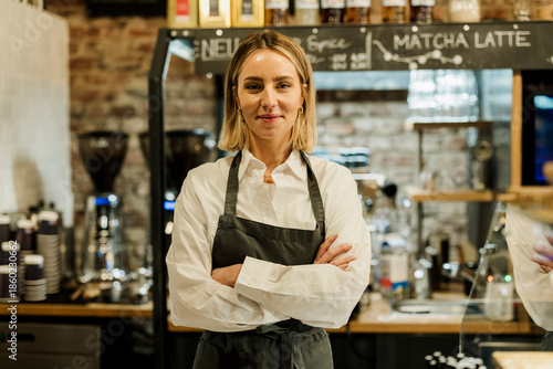 Barista in apron standing proudly in cozy cafe looking at camera