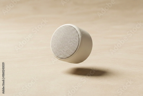 Minimalist round Bluetooth speaker hovering above a smooth beige surface with a soft shadow.