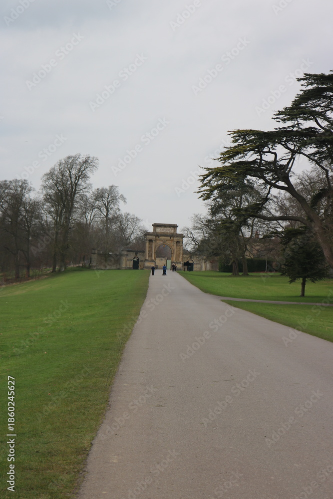 Fototapeta premium Straight Path Through a Green Park Leading to a Historic Stone Gate