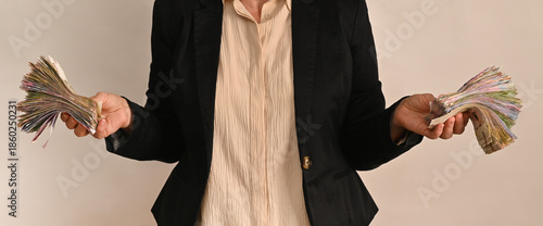 person wearing a black jacket holds stacks of banknotes in two hands, showing significant amount of money. woman holds cash in Ukrainian hryvnia.