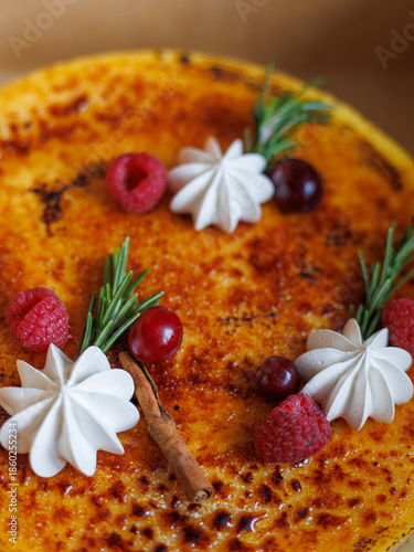 Homemade cheesecake decorated with cream, berries, cinnamon, and rosemary, close-up view. Concept of festive dessert background for baking, menu design, holiday marketing.