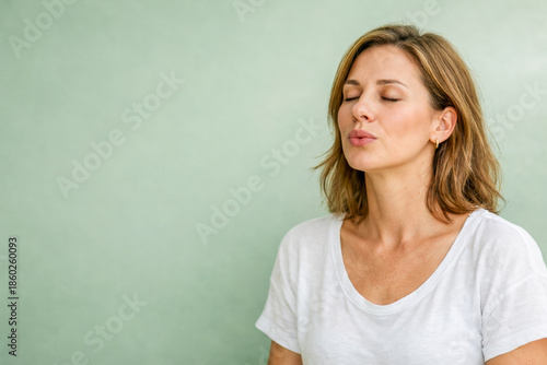 portrait of a woman practicing slow breathing with eyes closed against a soft green background, clean minimal colors and even light conveying focus, emotional regulation and mindful calm