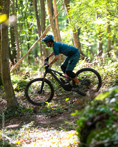 Mountain biker on an electric mountain bike riding through a sunlit forest trail