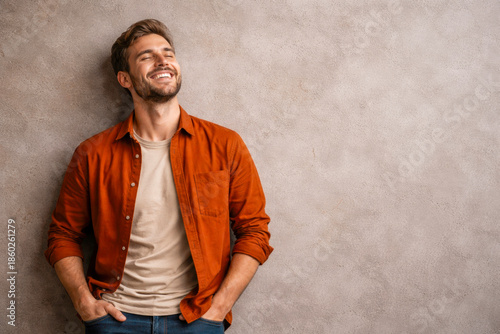 Horizontal photo of a smiling man leaning casually against a textured wall, warm earthy tones expressing optimism, relaxed confidence, and emotional lightness for states of mind, positive mindset