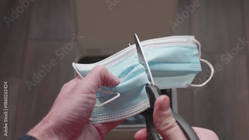 Man cutting a medical mask with scissors and throwing it into the trash bin. Concept of the end of the COVID-19 pandemic and returning to normal life.
