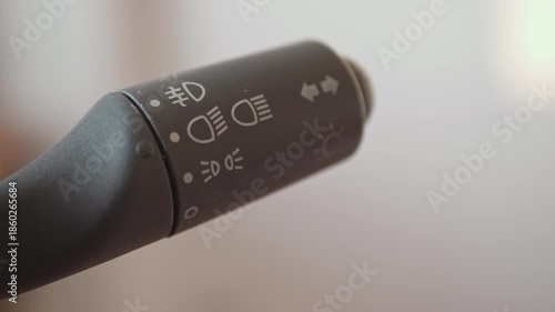 Close-up of a driver's hand operating a car light switch stalk to turn on headlights.