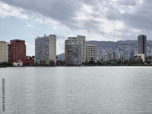 Quiet riverbank reflecting city skyline beneath cloudy sky