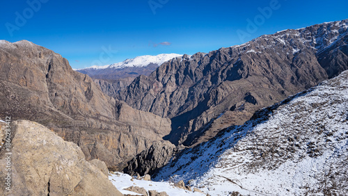 Quadro su tela Snow-dusted mountain canyon with rugged rocky slopes under a clear blue sky, showcasing remote wilderness, winter landscape, and dramatic natural terrain