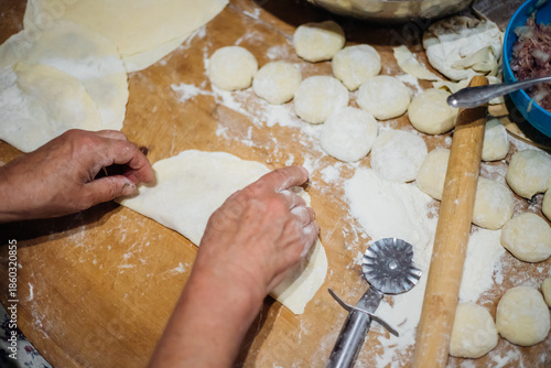 Close-up of an elderly woman's female hands rolling out dough with a wooden rolling pin. Making homemade pies and chebureks.