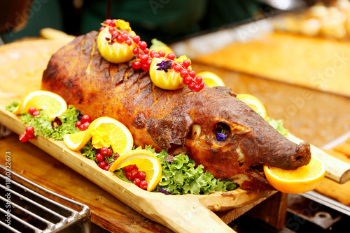 Grilled suckling piglet in spit roast. Traditional whole pig roasted on barbecue spit. Popular delicious and crispy roasted piggy on christmas fair