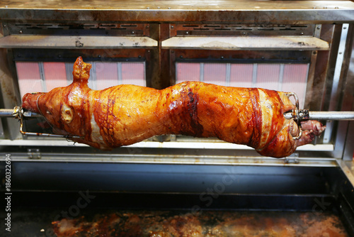 Grilled suckling piglet in spit roast. Traditional whole pig roasted on barbecue spit. Popular delicious and crispy roasted piggy on christmas fair