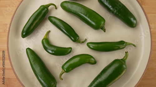 Green jalapeno peppers on plate rotation top view.
