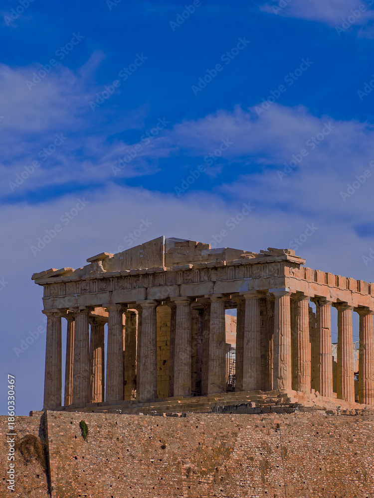 Fototapeta premium Parthenon, monumental symbol of Western civilization, stands atop the Acropolis hill against a vast, blue sky scattered with clouds, emphasizing the historical significance of the ancient structure.