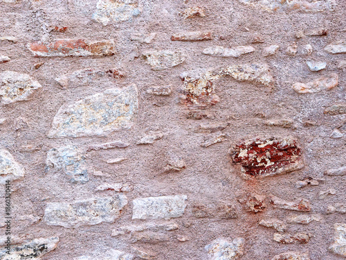 Traditional Mediterranean stone wall with a weathered, textured surface. The masonry features irregular natural stones embedded in a warm, earthy mortar, showcasing aged architectural character