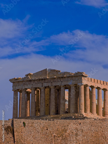 Parthenon, monumental symbol of Western civilization, stands  atop the Acropolis hill against a vast, blue sky scattered with clouds, emphasizing the historical significance of the ancient structure.
