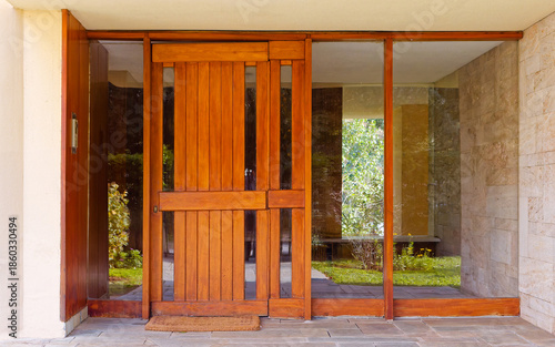 Contemporary entrance with a brown wood door set within expansive glass panels. Sophisticated blend of stone masonry, slate flooring, and warm minimalist design creates a seamless indoor-outdoor flow.