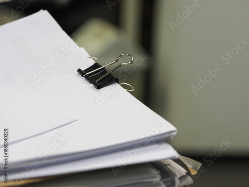 Stack of documents in focus with blurred office background, paperwork concept and shallow depth of field.