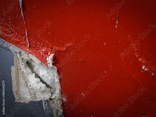 Close-up of cracked concrete wall with peeling red paint, rough texture and urban abstract detail.