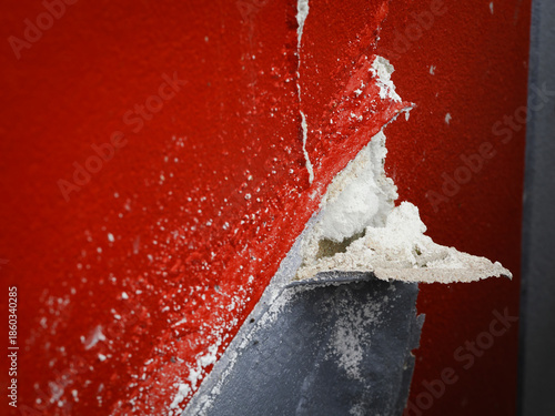Close-up of cracked concrete wall with peeling red paint, rough texture and urban abstract detail.