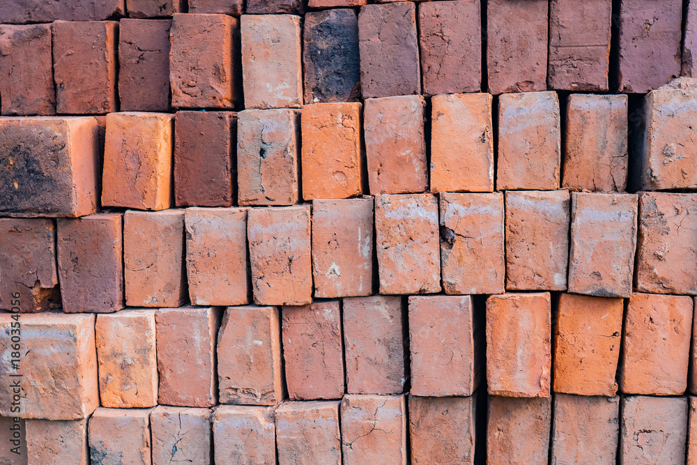 Fototapeta premium Pila ordenada de ladrillos de arcilla con textura áspera y tonos cálidos para construcción