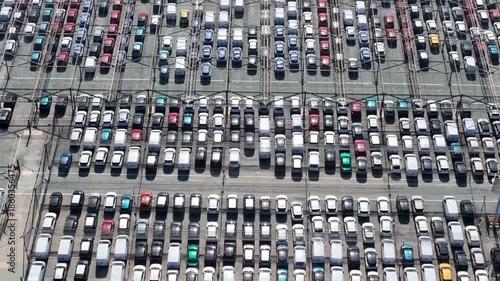Aerial view of a vast parking lot filled with rows of cars, creating a geometric pattern of light and shadow,