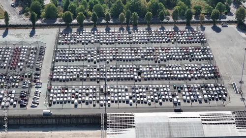 Aerial view of a vast parking lot filled with rows of cars, creating a geometric pattern of light and shadow,